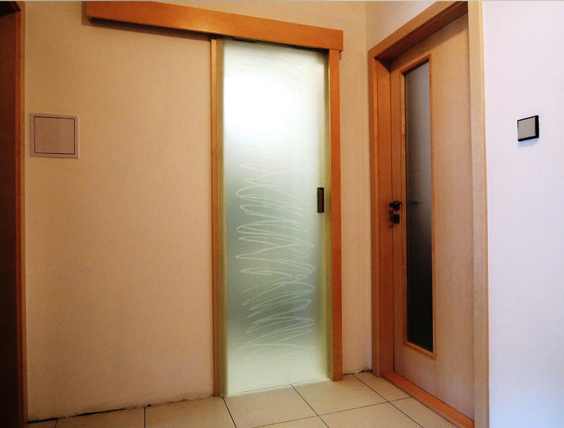 Interiérové dveře a obložková zárubeň, Celoskleněné dveře posuvné před stěnu, umístěné na dřevěné garnýži v dekoru osatatních dveří a zárubní. Sklo dekor S M40P, zárubeň přírodní dýha Bříza